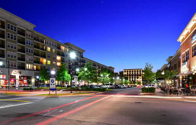 A city street at night with buildings on either side and cars driving down the road.