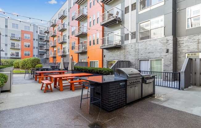 an outdoor patio with picnic tables and a grill in front of an apartment building at Bakery Living, Pittsburgh, PA