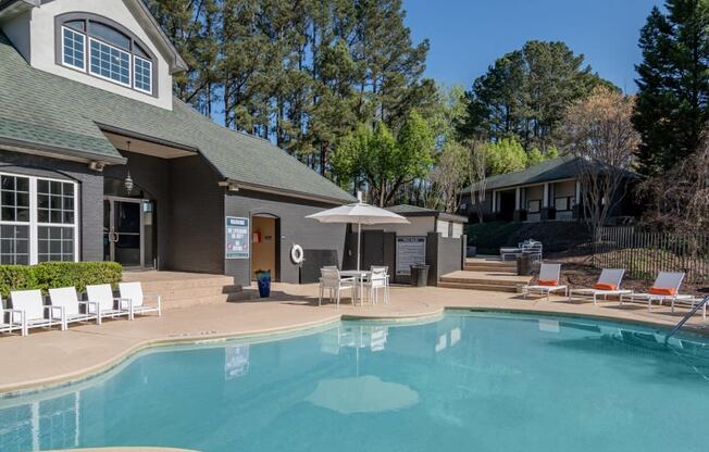 a swimming pool with chairs and umbrellas in front of a house