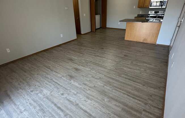 an empty living room with a kitchen in the background