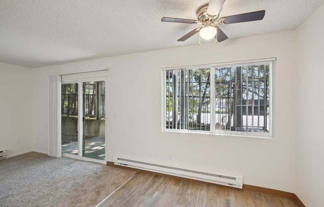 A room with a ceiling fan and a window with a view of trees.