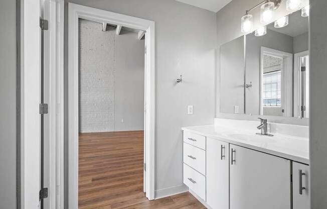 A bathroom with a white sink, mirror, and cabinets.
