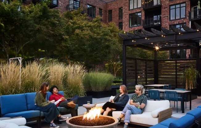 A group of people are sitting around a fire pit on a patio.