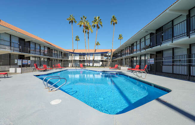 A swimming pool surrounded by red chairs and palm trees.