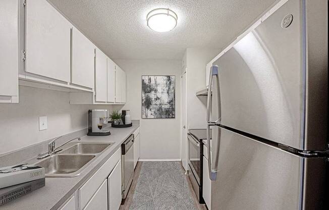 A kitchen with a sink, refrigerator, and cabinets.