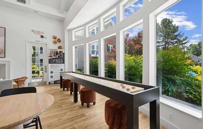 A room with a long table and chairs with a view of the backyard through the windows.