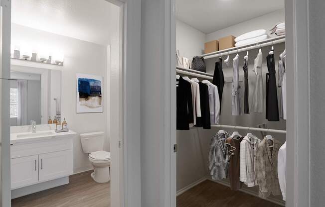 A white bathroom with a toilet, sink, and a closet with clothes.