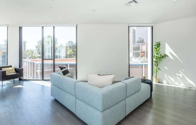 A light blue couch with a white pillow is in the middle of a room with a balcony outside.