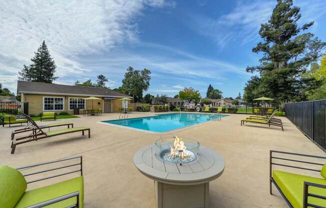 A poolside area with a fire pit in the middle of a concrete patio.