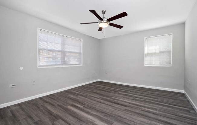 an empty room with a ceiling fan and two windows