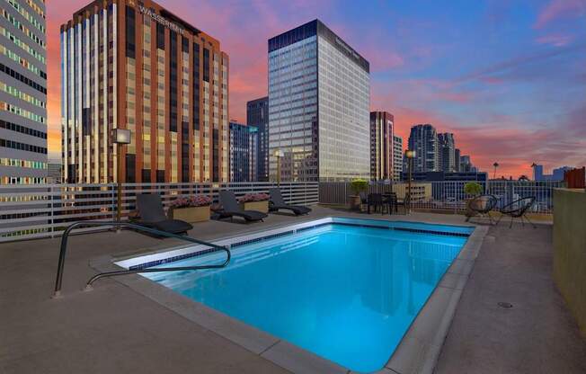 A swimming pool on a rooftop with a city skyline at sunset.