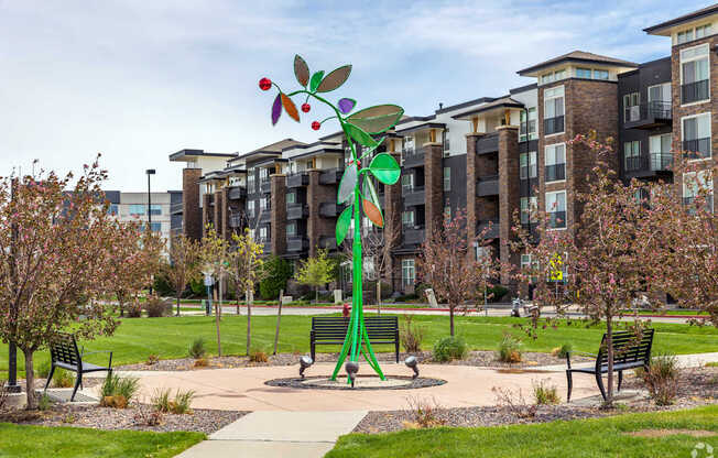 A playground with a large green and red tree-like structure in the middle of a grassy area.