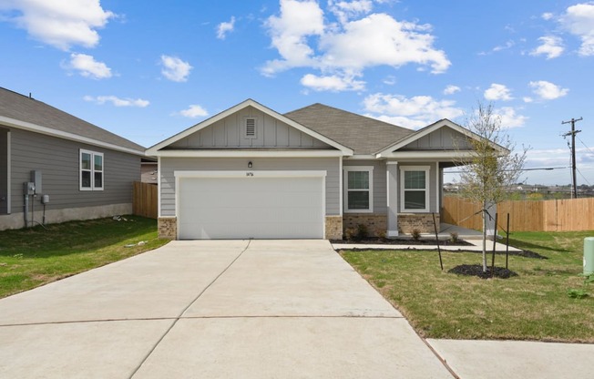 a house with a concrete driveway and a tree in the front yard at Beacon at Presidential Heights, Manor, TX