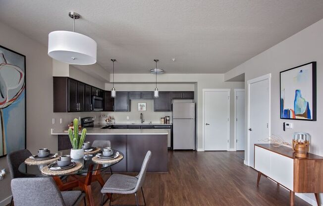 a dining area with a table and chairs and a kitchen in the background
