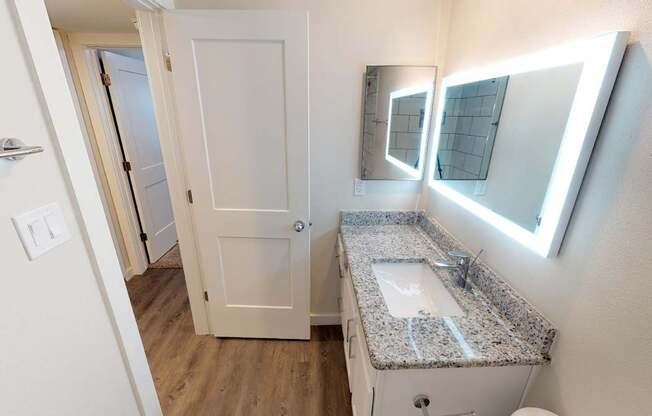 A bathroom with a granite counter top and a mirror with lights.