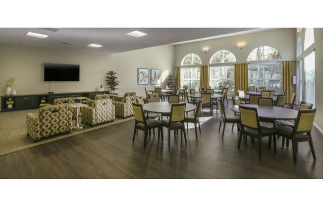 a large room with tables and chairs and a flat screen tv  at Tesoro Senior Apartments, Porter Ranch, CA