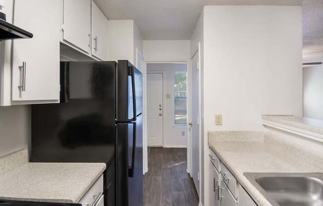 A black refrigerator in a kitchen with white cabinets.