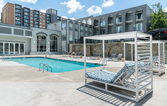 a pool with a chaise lounge chair in front of a building at The Heights Apartments, Cincinnati