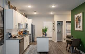 a kitchen and dining room with white cabinets and stainless steel appliances and a green wall