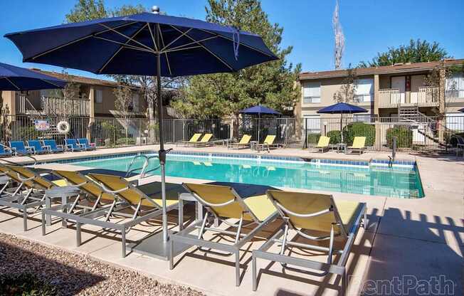 A pool with yellow chairs and blue umbrellas.