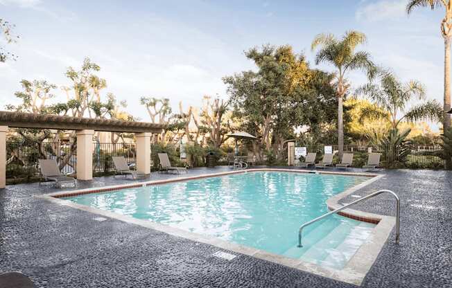 a swimming pool with chaise lounge chairs and trees in the background
