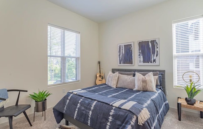 A bedroom with a bed, a chair, a guitar, and two potted plants.