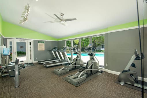Fitness center with cardio equipment and windows overlooking a swimming pool