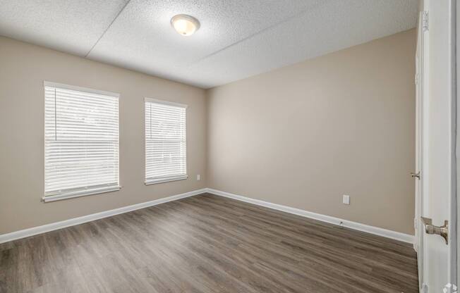 A room with wooden flooring and two windows.