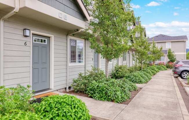 a sidewalk in front of a gray house with a blue door