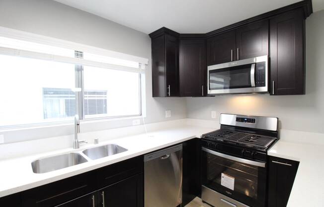 A kitchen with black cabinets and stainless steel appliances and a window