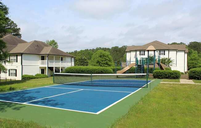A tennis court is surrounded by two houses.