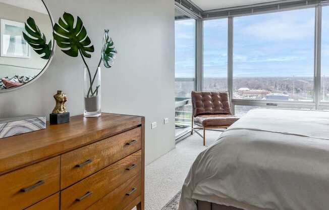 A bedroom with a large bed, a wooden dresser, and a view of the city.