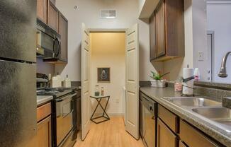 Kitchen with ceiling light, stainless steel appliances, dishwasher, oven, stove top, microwave, wood floor, closet room, and wood cabinets