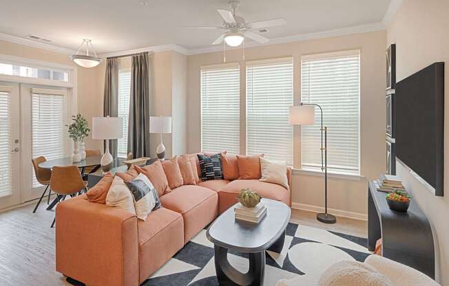 A living room with a large orange sofa and a flat screen TV mounted on the wall.
