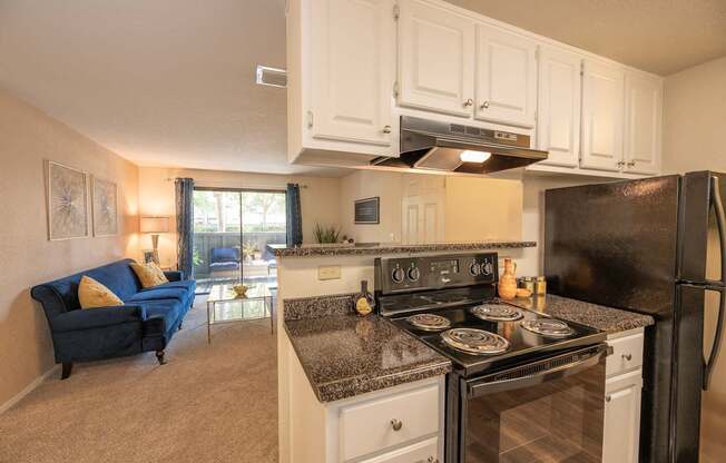 A kitchen with black appliances and a blue couch in the living room at Bishop's Court Apartments, California, 95670