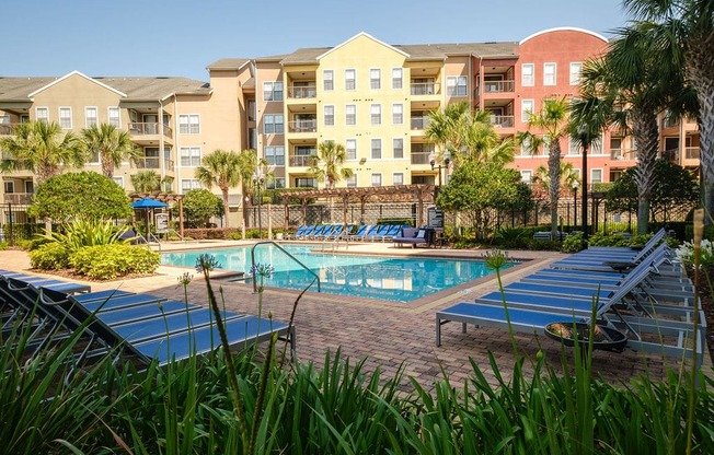 a swimming pool with blue lounge chairs in front of an apartment building