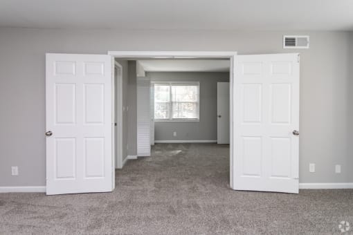 an empty living room with two white doors and a window