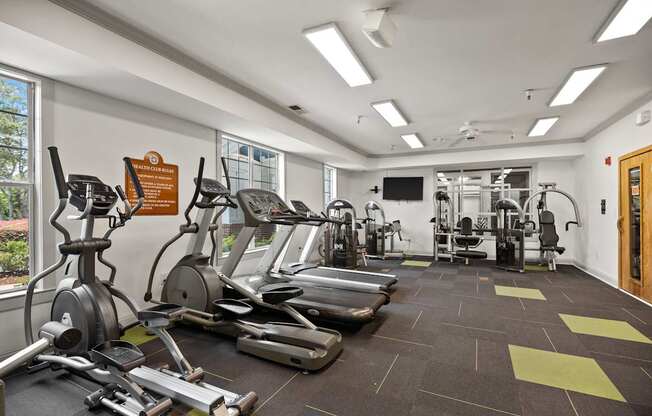 A gym with a variety of equipment including treadmills, weights, and a television.