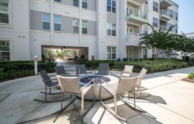 a patio with a firepit and chairs in front of an apartment building