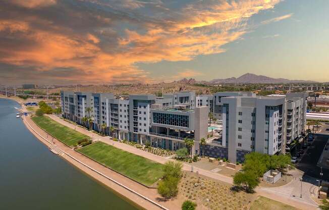 A modern apartment complex is situated along a riverbank with a mountain in the distance.