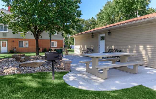 a patio with a picnic table and grill in front of a house