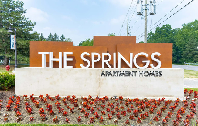a sign for the springs apartment homes with red flowers in front of it