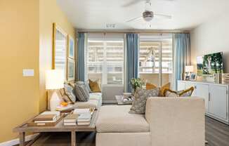 A living room with a beige sofa, a wooden coffee table, and a ceiling fan.