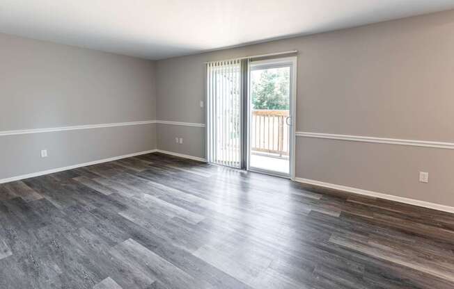 an empty living room with a sliding glass door to a balcony