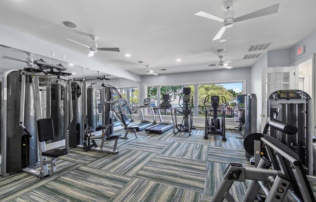 A gym with a variety of equipment including treadmills, weights, and a ceiling fan.