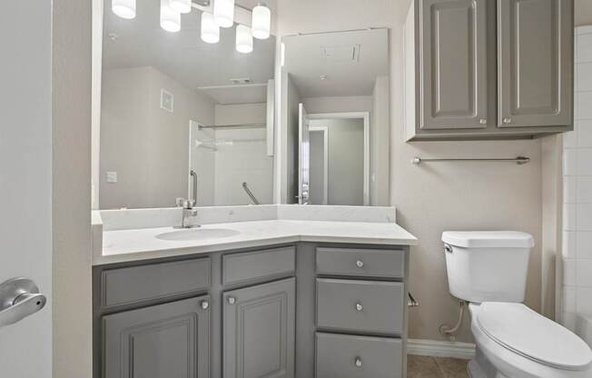 Kenzington bathroom with a white toilet and a sink with a mirror above it at Encore at Buckingham Apartments in Richardson, TX