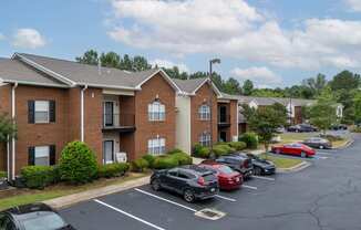 a parking lot in front of a brick apartment building with cars parked in front