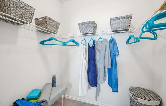 A white closet with clothes hanging and baskets on the shelf.