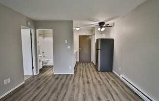 an empty living room with a refrigerator and a ceiling fan