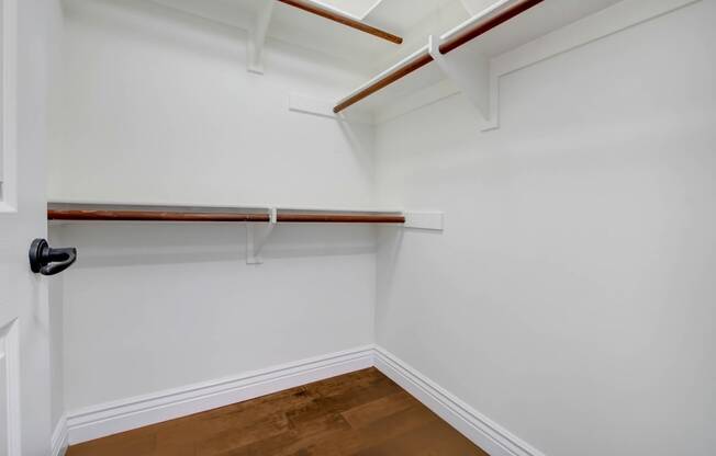 a walk in closet with white walls and a wood floor